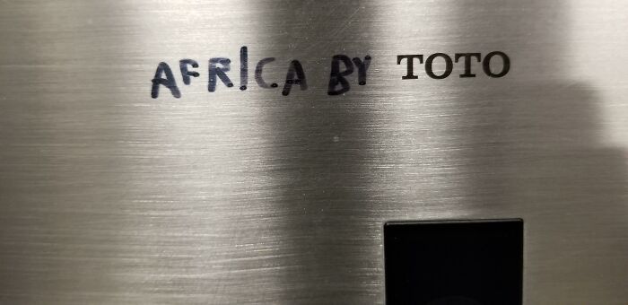 Clever vandalism on a toilet fixture with hand-drawn letters spelling Africa next to Toto