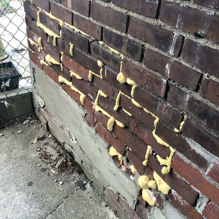 A brick wall messily patched with yellow expanding foam, demonstrating a botched home renovation job.
