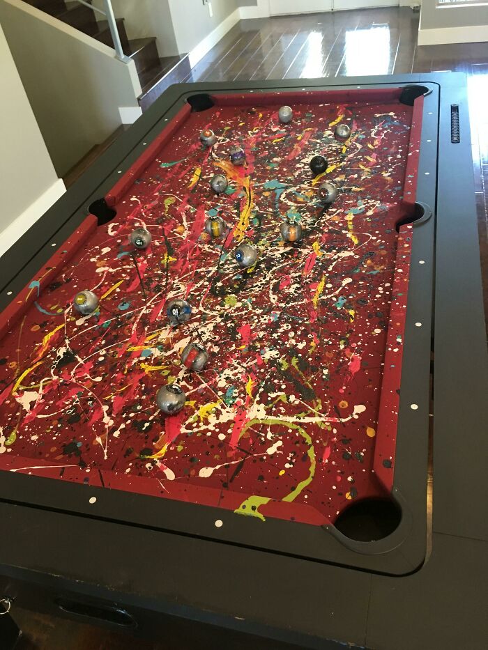 A pool table painted with messy paint splatters, illustrating a DIY home renovation mishap.
