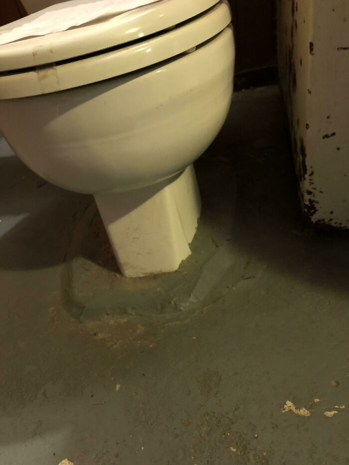 A poorly installed toilet sealed with a thick ring of gray cement, a complete fiasco of a bathroom repair.