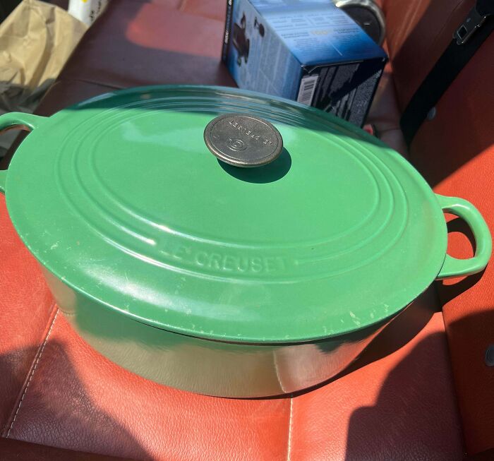 A green Le Creuset Dutch oven on a car seat, a lucky discovery among thrift store finds.
