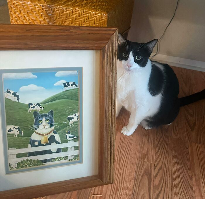 A black and white cat posing next to a cat painting, showcasing great thrift store finds.