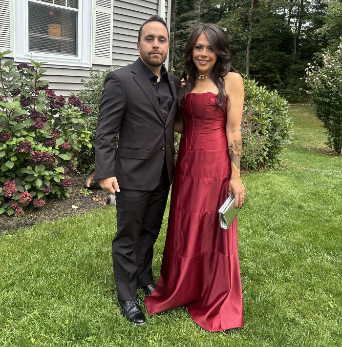 A couple posing outdoors, with the woman wearing a stunning red satin dress, one of many great secondhand finds.