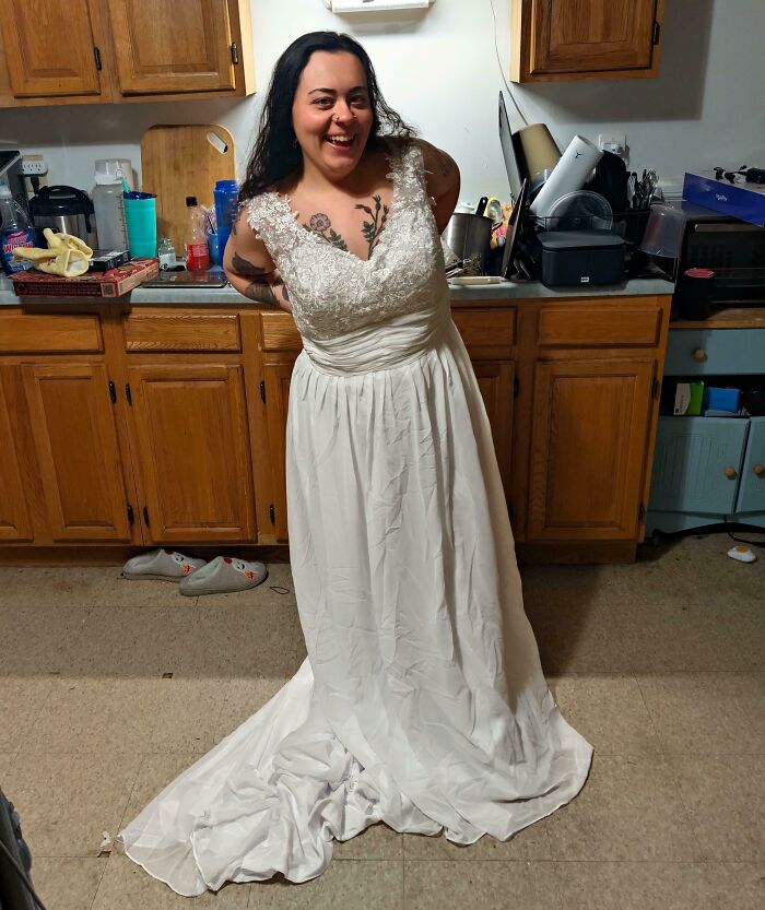 Smiling woman trying on a white lace wedding dress found at a secondhand thrift store.