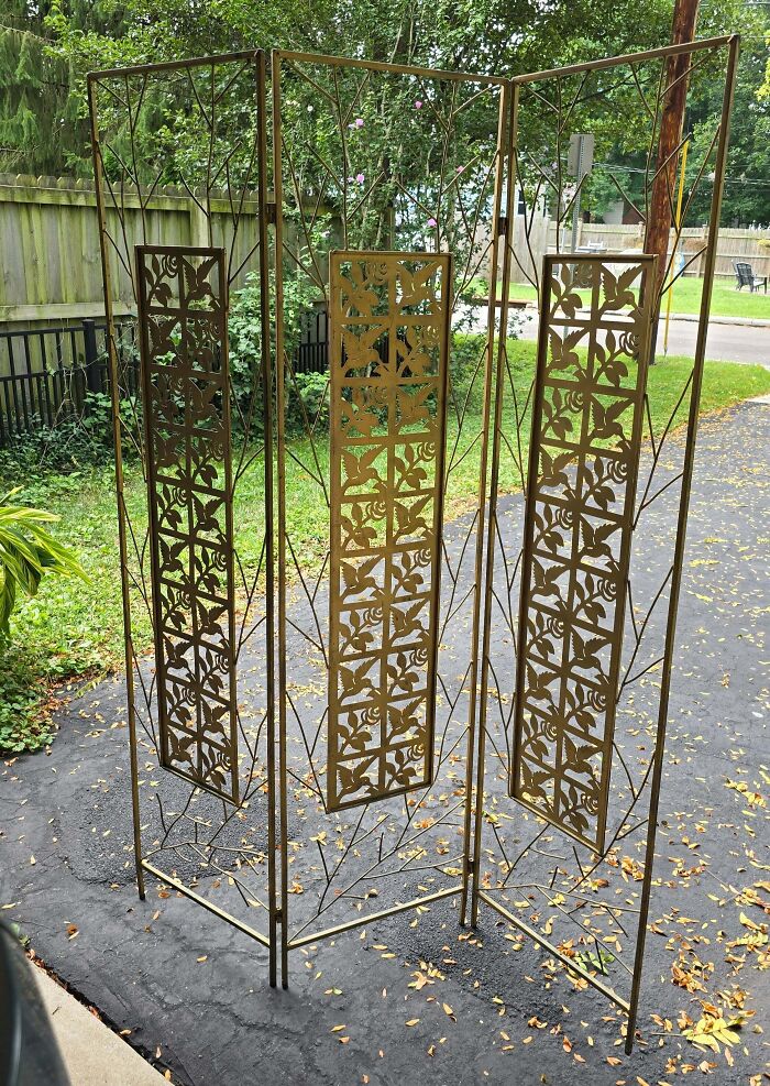 An ornate, gold-painted metal room divider screen standing on a driveway, a rare secondhand find.