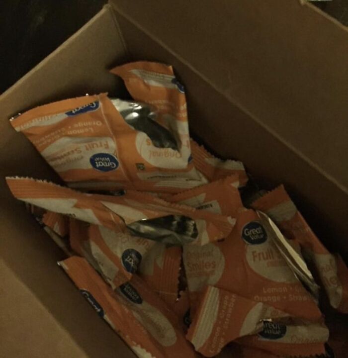 Cardboard box filled with empty, opened snack wrappers reflecting funny roommate stories.