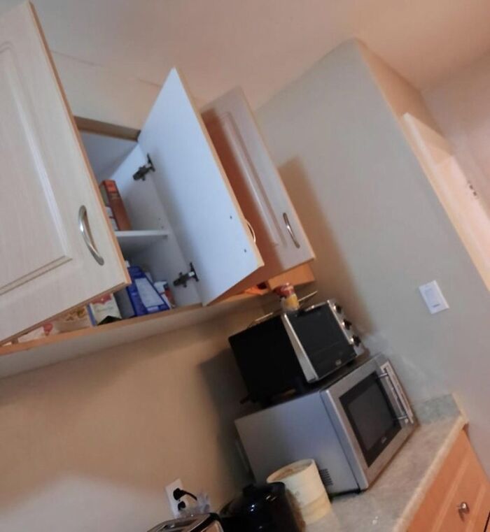 Open kitchen cabinet doors above a microwave, highlighting typical roommate stories and habits.