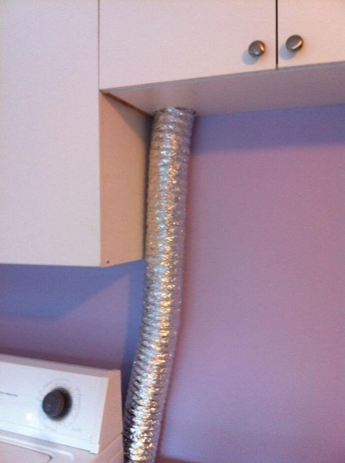 A flexible silver vent pipe awkwardly squeezed between white kitchen cabinets, illustrating a poor choice to renovate their homes.