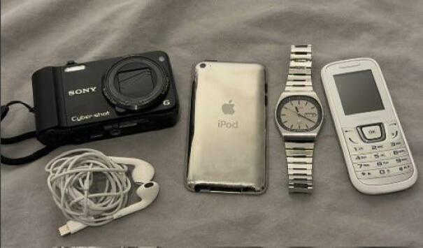 An assortment of vintage tech including a Sony camera, Apple iPod, metal wrist watch, and a white Nokia phone.