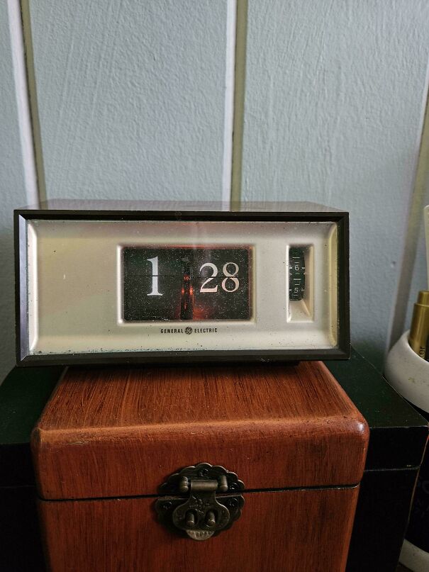 A vintage General Electric digital flip alarm clock sits atop a wooden box, showing retro tech design