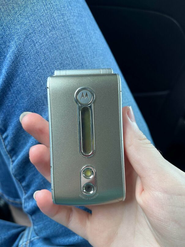 A hand holding a classic silver flip phone representing vintage tech finds