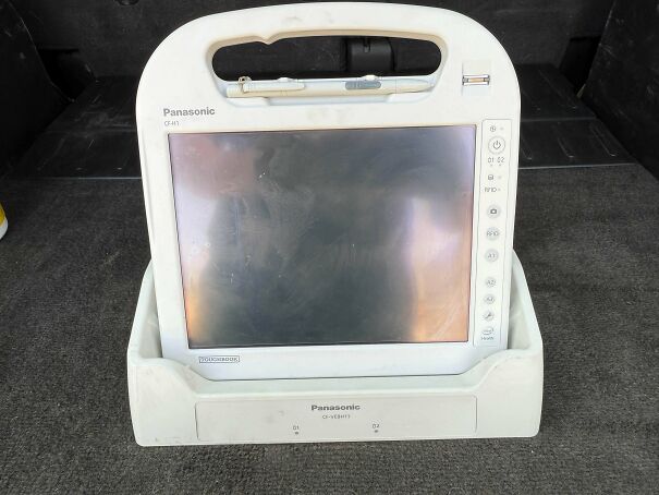 A rugged white Panasonic Toughbook tablet resting on its vintage tech docking station