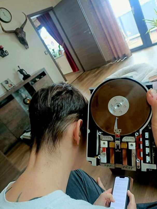 A person comparing a modern smartphone with a giant vintage tech hard drive