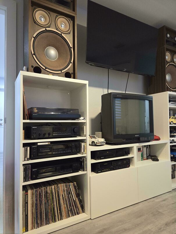 An entertainment center filled with vintage tech, including a CRT TV, a record player, and large wooden speakers.