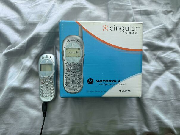 A retro Motorola Cingular wireless mobile phone alongside its original blue retail box on a fabric surface