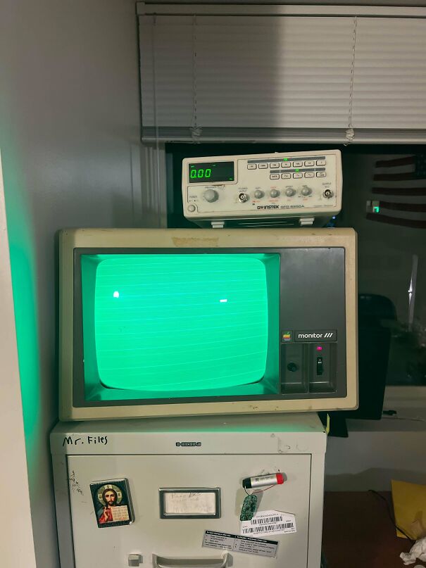 An old Apple Monitor III screen glowing green on top of a filing cabinet representing vintage tech