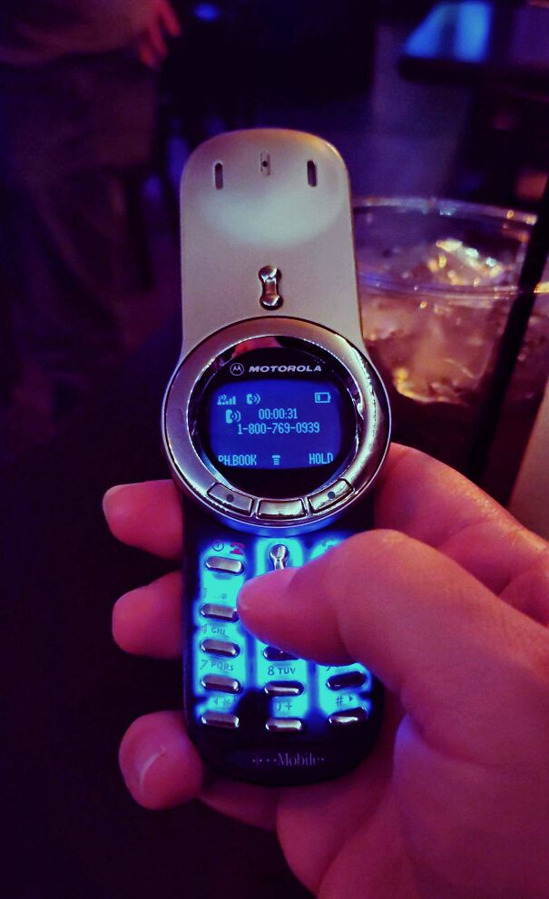 A person holding an old-school Motorola mobile phone featuring classic buttons and a blue backlit screen