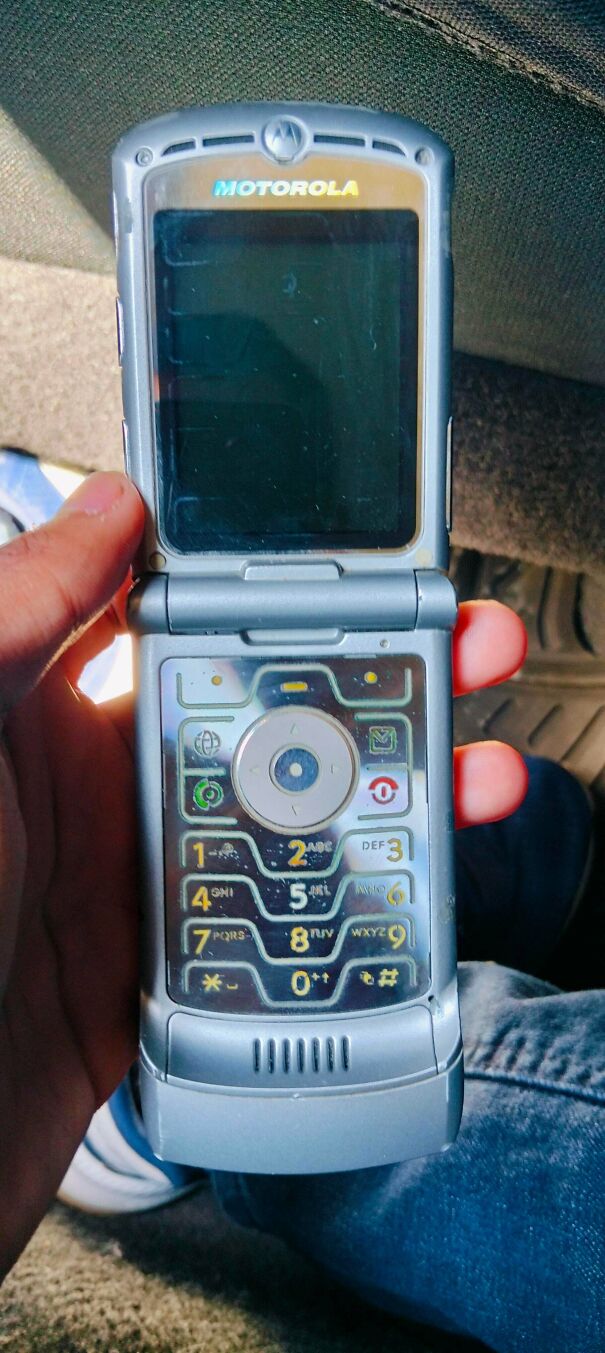 A hand holding a classic silver Motorola flip phone, a popular piece of vintage tech.