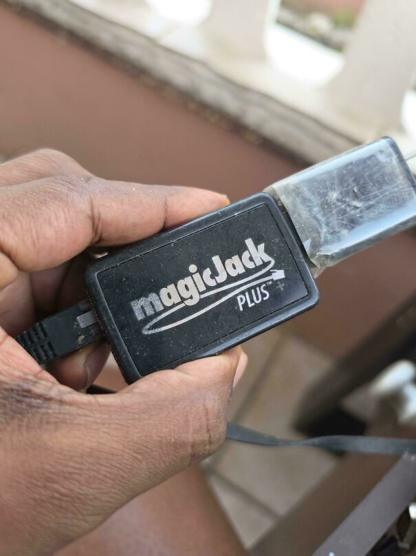 A hand holding a black magicJack Plus, a piece of vintage tech used for making phone calls over the internet.