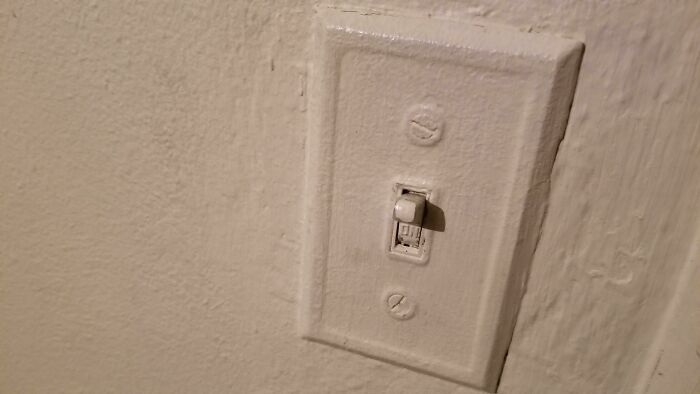 A light switch painted over completely with thick white paint illustrating questionable decisions in home DIY.