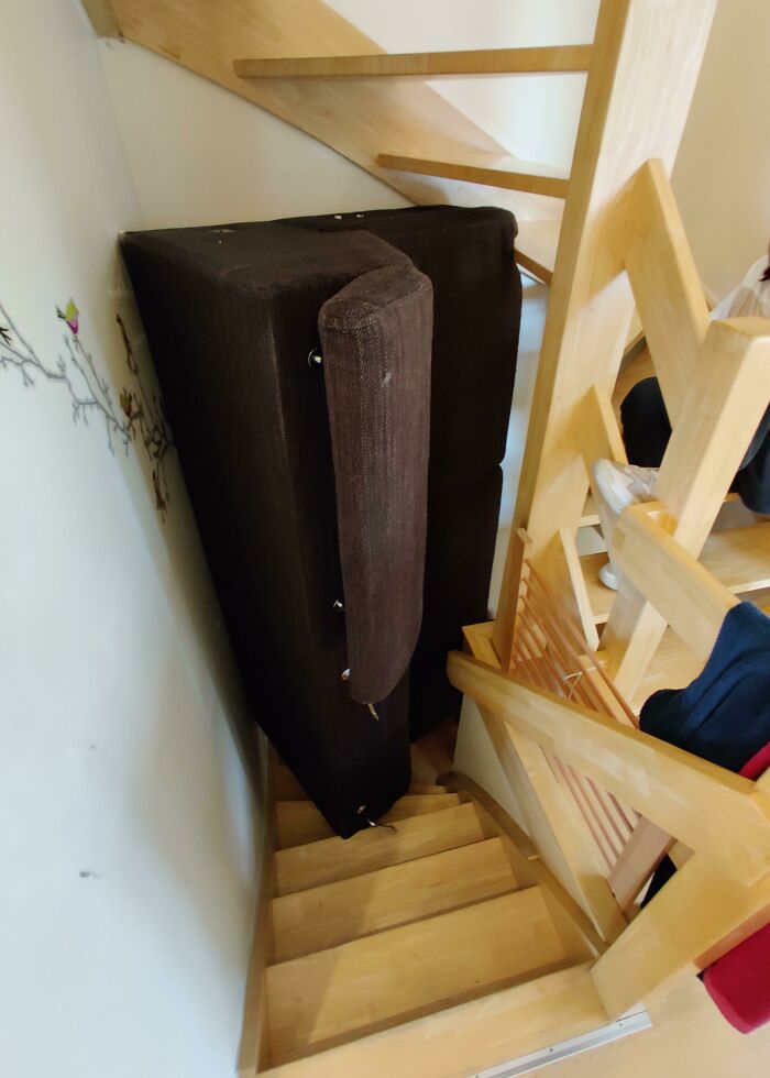 A brown sofa wedged in a tight wooden staircase, showing questionable decisions.