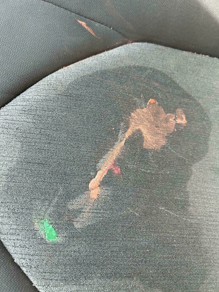 A grey car seat stained with orange and green spills, illustrating questionable decisions in car maintenance.