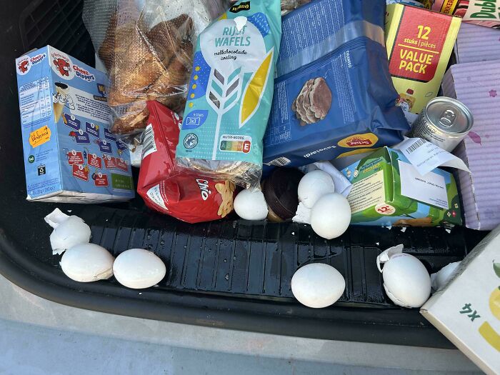 Loose white eggs rolling around the trunk of a car next to groceries, showcasing questionable decisions.