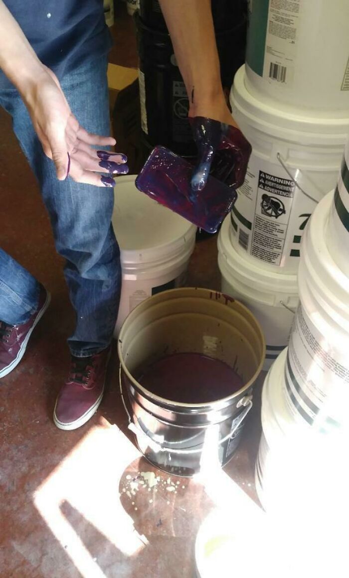 A questionable decision resulting in a smartphone covered in thick purple paint held above a paint bucket