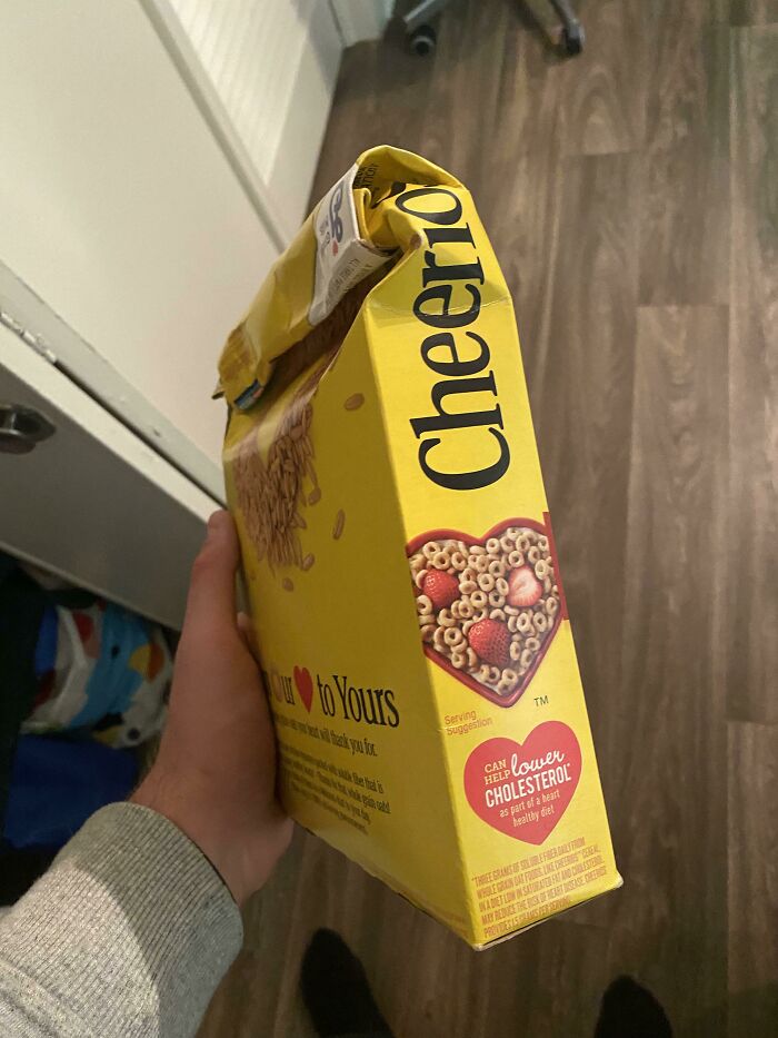 A hand holding a cereal box crushed from the side instead of open from the top, a questionable decision.
