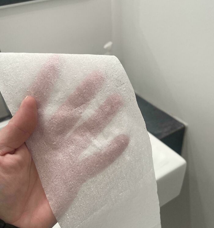 Extremely thin and transparent single-ply toilet paper held up to show a hand underneath