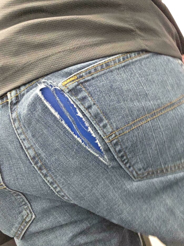 Close-up of a person wearing jeans with a large rip next to the pocket, showing questionable choices