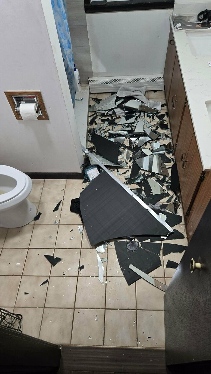 Shards of a shattered bathroom mirror scattered across a tiled bathroom floor
