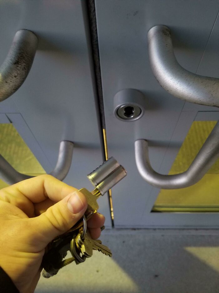A hand holding a key ring with the entire lock cylinder pulled out of the door, a questionable decision