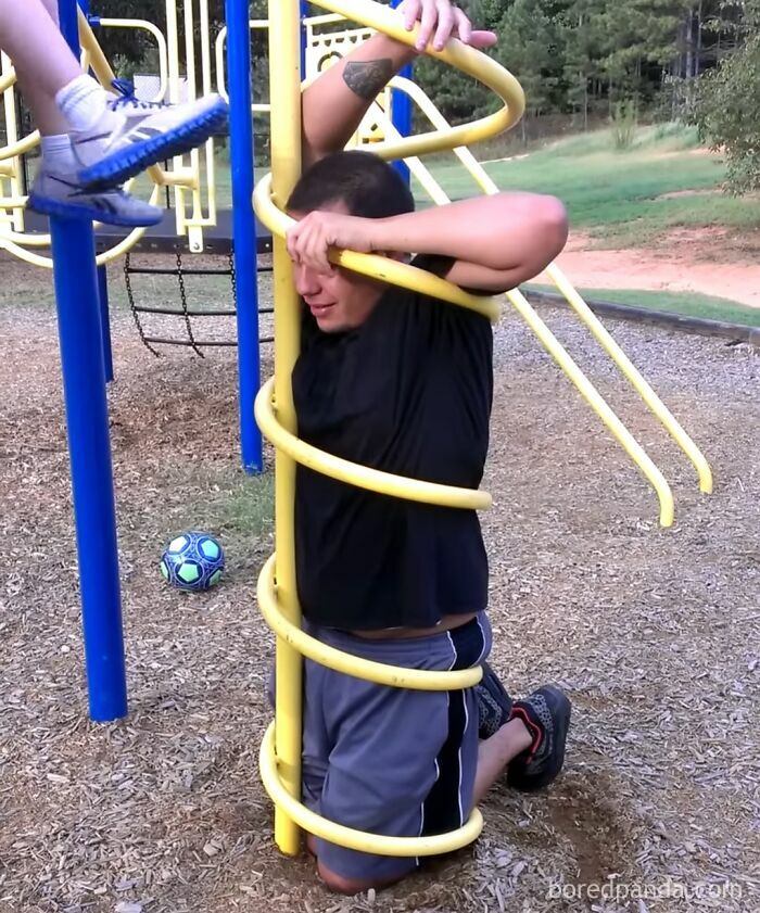 A man stuck inside a yellow spiral climber on a playground, illustrating questionable decisions in adult play.
