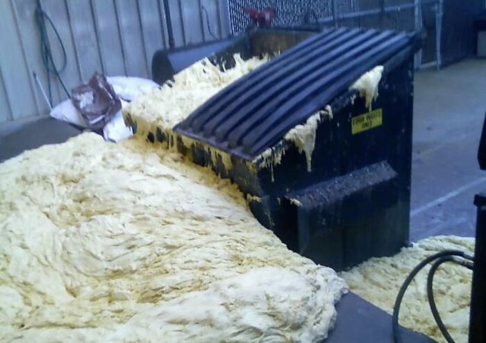 A black dumpster overflowing with a massive pile of rising bread dough, showing questionable decisions.