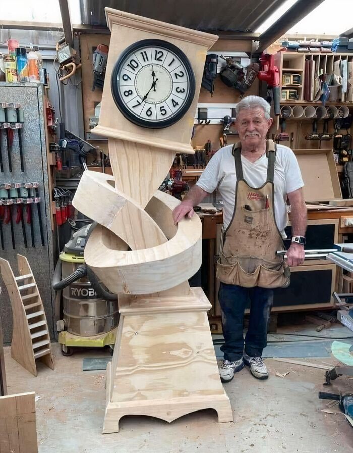 A carpenter stands next to a whimsical grandfather clock with a knotted wooden body, among clever wooden creations