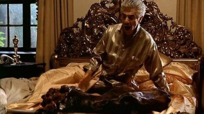 Man screaming in bed next to a prosthetic horse head, classic movie props.