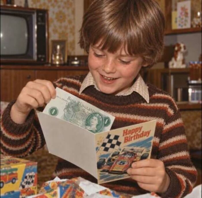 Boy opening a 1970s birthday card with cash inside in a cozy retro living room