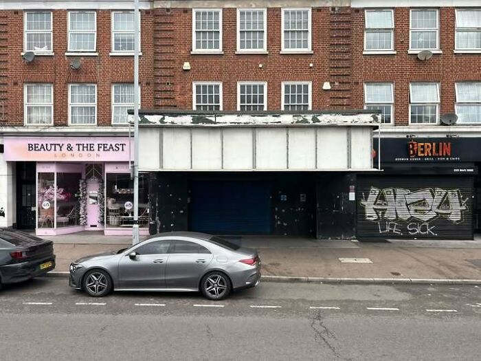 Empty 70s London street with worn storefronts and parked cars