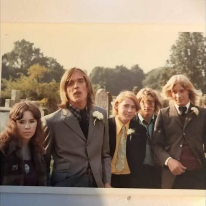 Group of young people dressed in 1970s style suits and dresses posing outdoors
