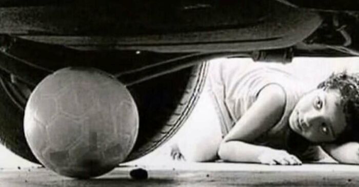 A young child reaching for a soccer ball under a car in vintage black and white 70s photos.