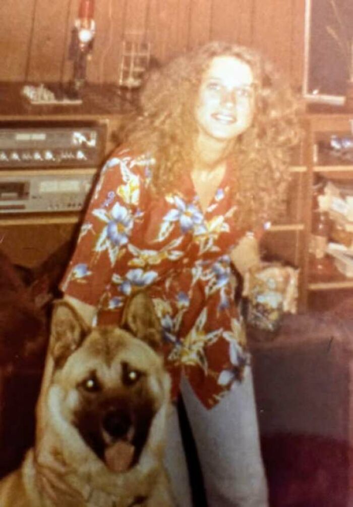 Person in 70s floral shirt kneeling with dog inside home