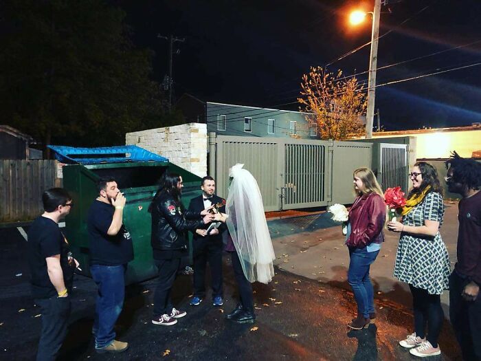 Bride and groom with guests standing near a green dumpster, showing questionable wedding moments.