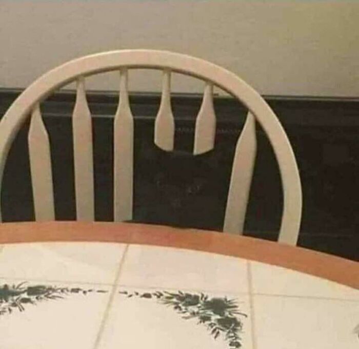 A black cat hiding behind a wooden chair, an example of accidental camouflage with the dark background.