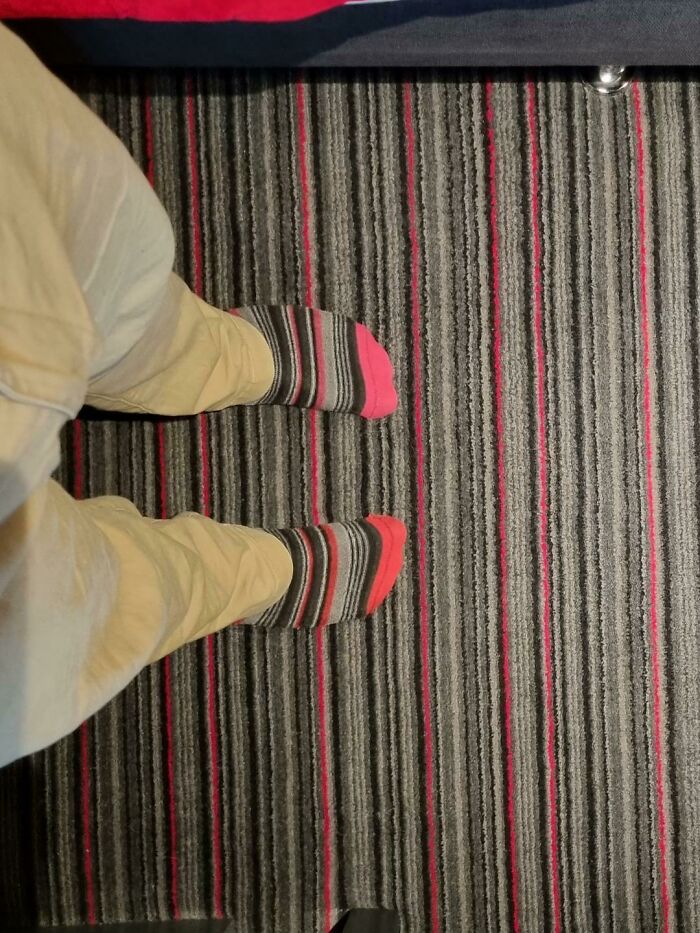 Feet wearing striped socks that align perfectly with the striped floor carpet, an accidental camouflage