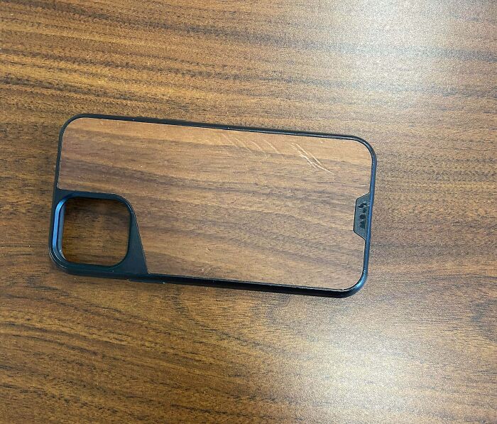 A wood grain phone case displaying accidental camouflage by blending in with a wooden desk