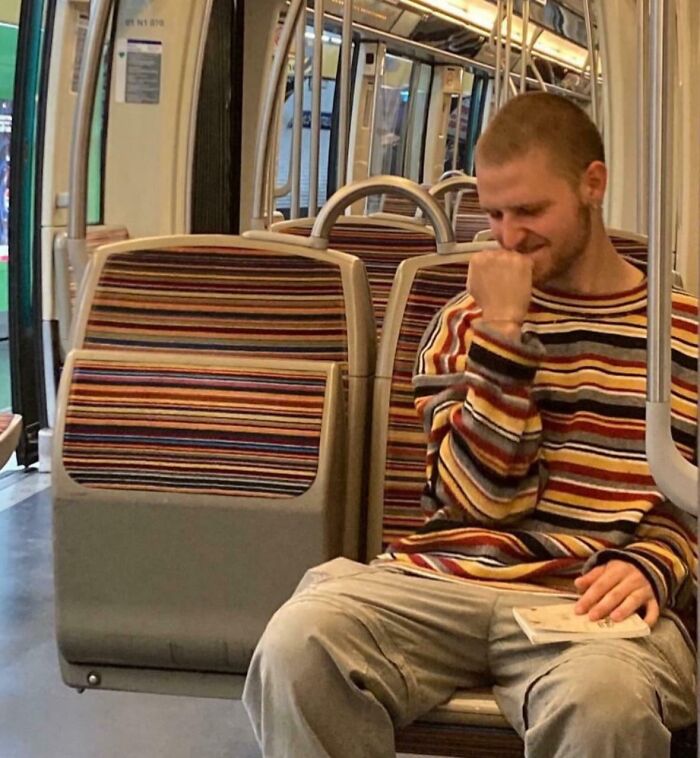 Man on public transit wearing striped sweater that blends with the seat pattern, a case of accidental camouflage