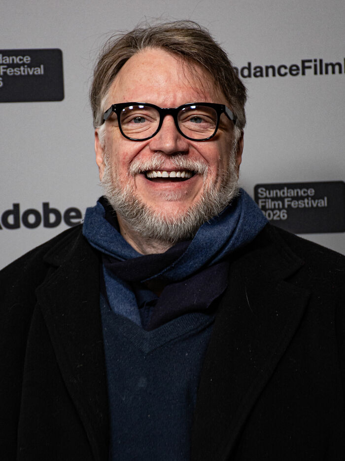 Filmmaker Guillermo del Toro smiling warmly in a black coat and blue scarf at a film festival event