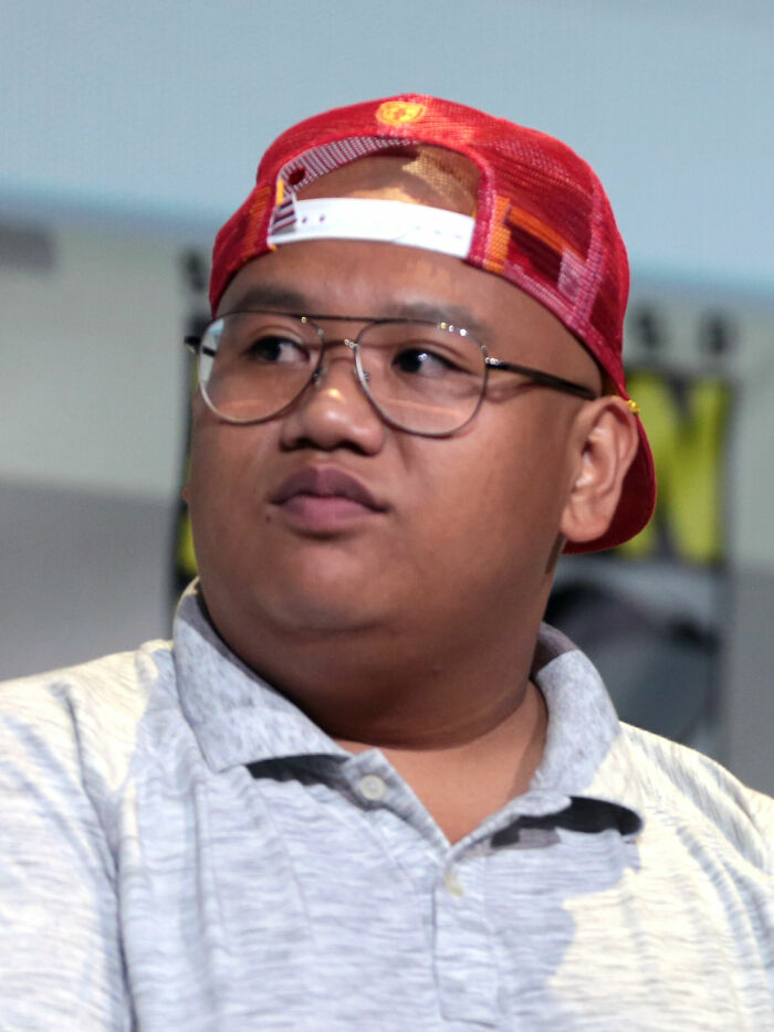Actor Jacob Batalon wearing glasses and a red cap at an event