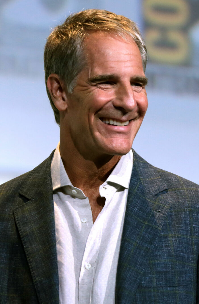 Actor Scott Bakula smiling during a public career highlights event in a grey suit jacket and white shirt